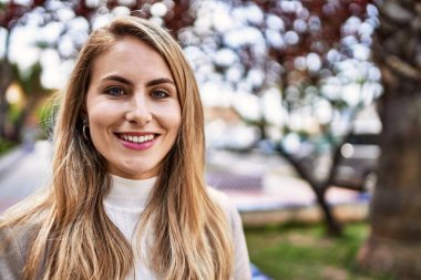 Parkta kendinden emin gülümseyen genç sarışın kadın.