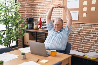 Orta yaşlı, kır saçlı bir iş adamı ofiste dizüstü bilgisayar kullanıyor.