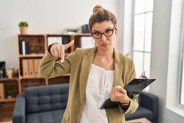 Muayenehanede çalışan genç bir kadın üzgün ve üzgün görünüyor, parmaklarıyla yön gösteriyor, mutsuz ve depresif.. 