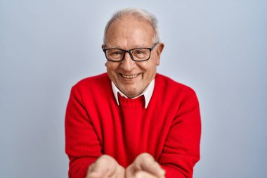 Senior man with grey hair standing over isolated background smiling with hands palms together receiving or giving gesture. hold and protection 