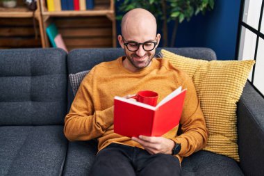 Genç adam kitap okuyor ve evde kahve içiyor.