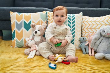 Sevimli kızıl saçlı bebek evdeki kanepede oturmuş oyuncak arabasıyla oynuyor.