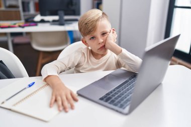 Sınıftaki masada dizüstü bilgisayar kullanan sevimli, yeni yetme bir öğrenci.