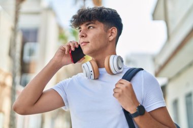 Young hispanic teenager student talking on smartphone with relaxed expression at street