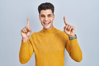 Mavi arka planda duran genç İspanyol adam şaşırmış, şaşırmış ve parmaklarıyla işaret ediyor ve kollarını kaldırıyordu.. 