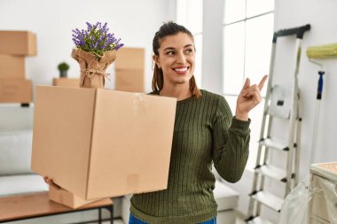 Genç İspanyol kadın hareket halindeyken karton kutu tutuyor gülümsüyor mutlu bir şekilde elini ve parmağını yana uzatıyordu. 