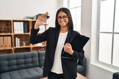 Young hispanic woman working at consultation office holding sand clock winking looking at the camera with sexy expression, cheerful and happy face. 