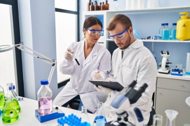 Man and woman scientist partners write on clipboard holding test tube working at laboratory