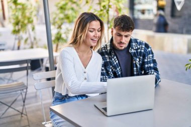 Genç bir adam ve kadın kahve dükkanının terasında dizüstü bilgisayar kullanıyorlar.