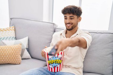 Young arab man eating popcorn watching movie at home