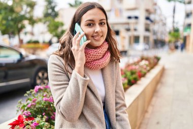 Young beautiful hispanic woman talking on smartphone wearing scarf at street
