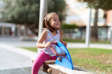 Adorable hispanic girl sitting on swing playing at park playground