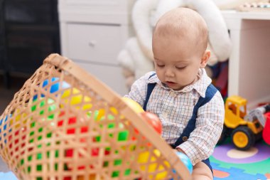 Sevimli beyaz bebek anaokulunda yerde taşaklarıyla oynuyor.