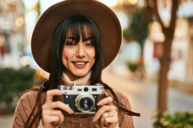 Kışlık şapkalı esmer kadın şehrin dışında klasik kamera kullanarak gülümsüyor.