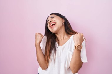 Young arab woman standing over pink background celebrating surprised and amazed for success with arms raised and eyes closed. winner concept. 