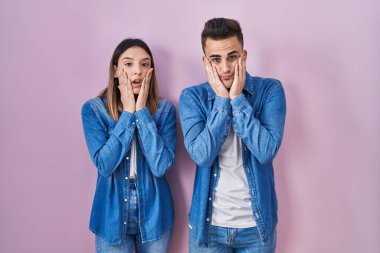 Young hispanic couple standing over pink background tired hands covering face, depression and sadness, upset and irritated for problem 