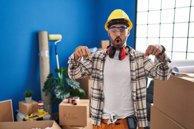 Evde sakallı ve sakallı genç bir adam ev tadilatında çalışıyor. İlan veren parmaklarıyla işaret ediyor. Şaşırmış yüz ve ağzı açık. 