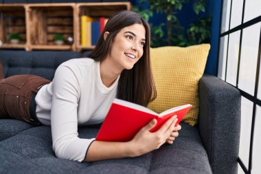 Evdeki kanepede uzanmış kitap okuyan güzel İspanyol kadın.