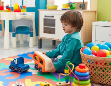 Adorable toddler playing with truck toy sitting on floor at kindergarten