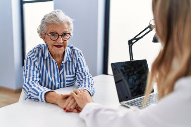Kıdemli gri saçlı kadın hasta klinikte elleri ile tıbbi danışmanlık yapıyor.