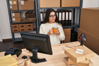 Young hispanic woman ecommerce business worker drinking coffee at office