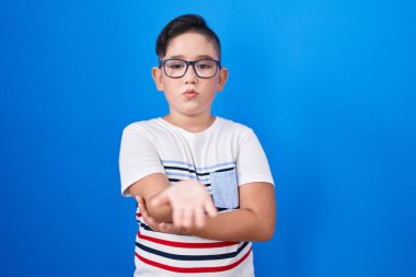 Young hispanic kid standing over blue background looking at the camera blowing a kiss with hand on air being lovely and sexy. love expression. 