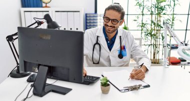 Handsome hispanic man working as doctor using clipboard at hospital clinic