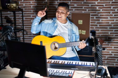 Latin asıllı genç adam müzik stüdyosunda klasik gitar çalıyor. Şaşırmış, şaşırmış ve parmaklarıyla işaret ediyor ve kollarını kaldırıyor.. 