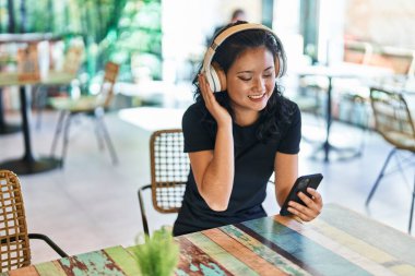 Young chinese woman using smartphone and headphones sitting on table at restaurant