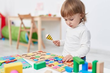 Adorable hispanic girl playing with maths puzzle game standing at kindergarten