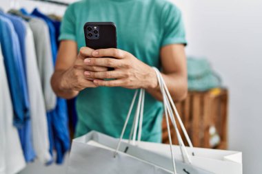 Genç Arap müşteri giyim mağazasında akıllı telefon kullanıyor.