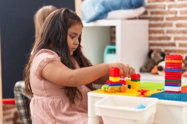 Plus size hispanic girl playing with construction blocks sitting on table at kindergarten