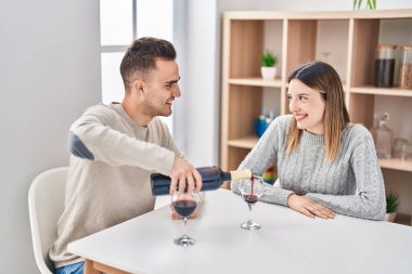 Man and woman couple drinking pouring red wine on glass at home