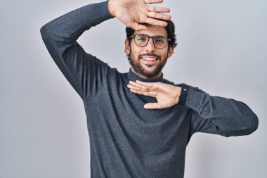 Handsome latin man standing over isolated background smiling cheerful playing peek a boo with hands showing face. surprised and exited 
