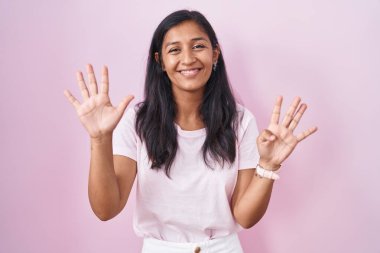 Pembe arka planda duran genç İspanyol kadın dokuz numarayı gösterip işaret ederken kendinden emin ve mutlu bir şekilde gülümsüyor.. 