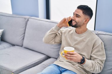 Genç Arap adam kahve içiyor ve evde akıllı telefondan konuşuyor.