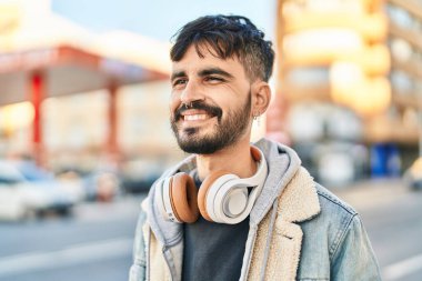 Sokakta kulaklık takarak gülümseyen İspanyol genç adam.