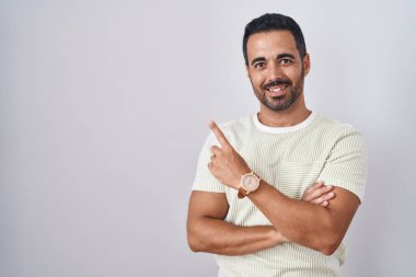 Sakallı İspanyol bir adam izole edilmiş arka planda duruyor. Yüzünde kocaman bir gülümseme var. Parmağıyla kameraya bakıyor.. 