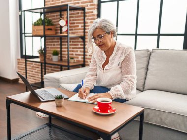 Orta yaşlı bir kadın evde dizüstü bilgisayar kullanarak ders çalışıyor.