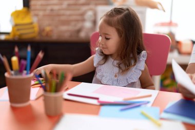 Anaokulunda masaya oturmuş kağıda resim çizen sevimli İspanyol kız öğrenci.