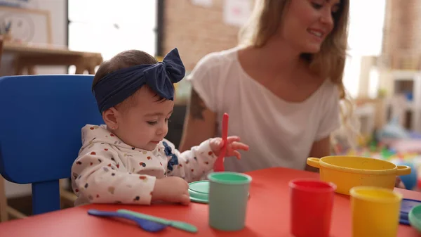 유치원 식탁에 플라스틱 장난감을 가지고 식사하는 배우는 여자와 아기들 — 스톡 사진