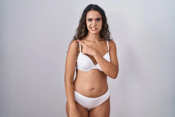Young hispanic woman wearing white lingerie pointing aside worried and nervous with forefinger, concerned and surprised expression