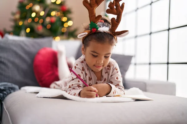 Adorable Hispanic Girl Drawing Notebook Lying Sofa Christmas Tree Home — 스톡 사진