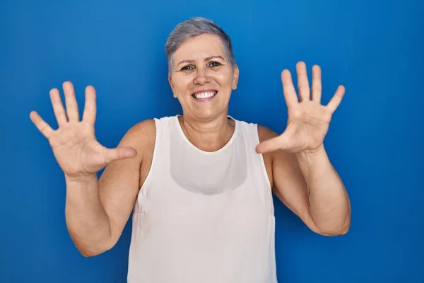 中年的高加索女人站在蓝色的背景上 用十号手指指指着 自信而快乐地微笑着 — 图库照片