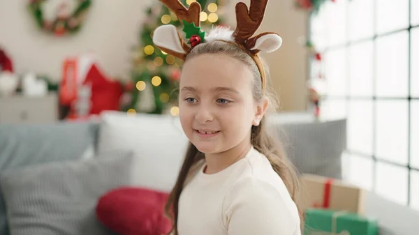 愛らしいHispanic女の子身に着けているトナカイ耳座っています上のソファによってクリスマスツリーホーム — ストック写真