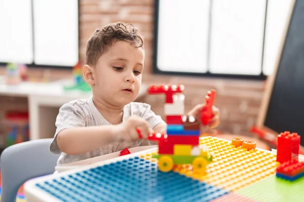 Adorable hispanic toddler playing with construction blocks sitting on table at kindergarten