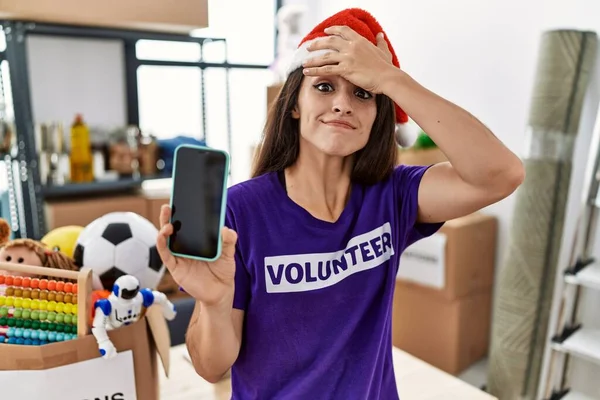 Молодая Брюнетка Футболке Волонтера Рождественской Шляпе Показывает Экран Смартфона Напряженным — стоковое фото
