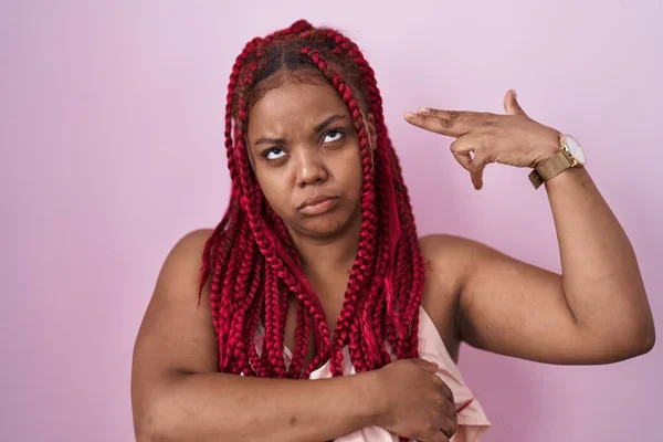 African american woman with braided hair standing over pink background shooting and killing oneself pointing hand and fingers to head like gun, suicide gesture.