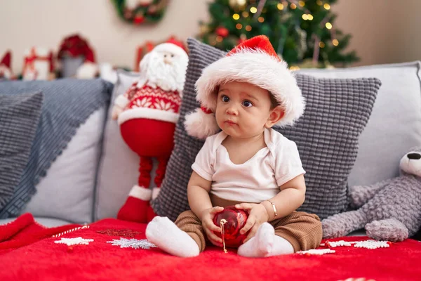 Adorable Hispanic Baby Holding Christmas Decoration Ball Sitting Sofa Home — Stock Photo, Image