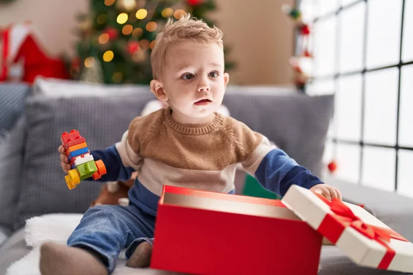 Αξιολάτρευτο Νήπιο Ξεπακετάρισμα Χριστουγεννιάτικο Δώρο Κάθεται Στον Καναπέ Στο Σπίτι — Φωτογραφία Αρχείου